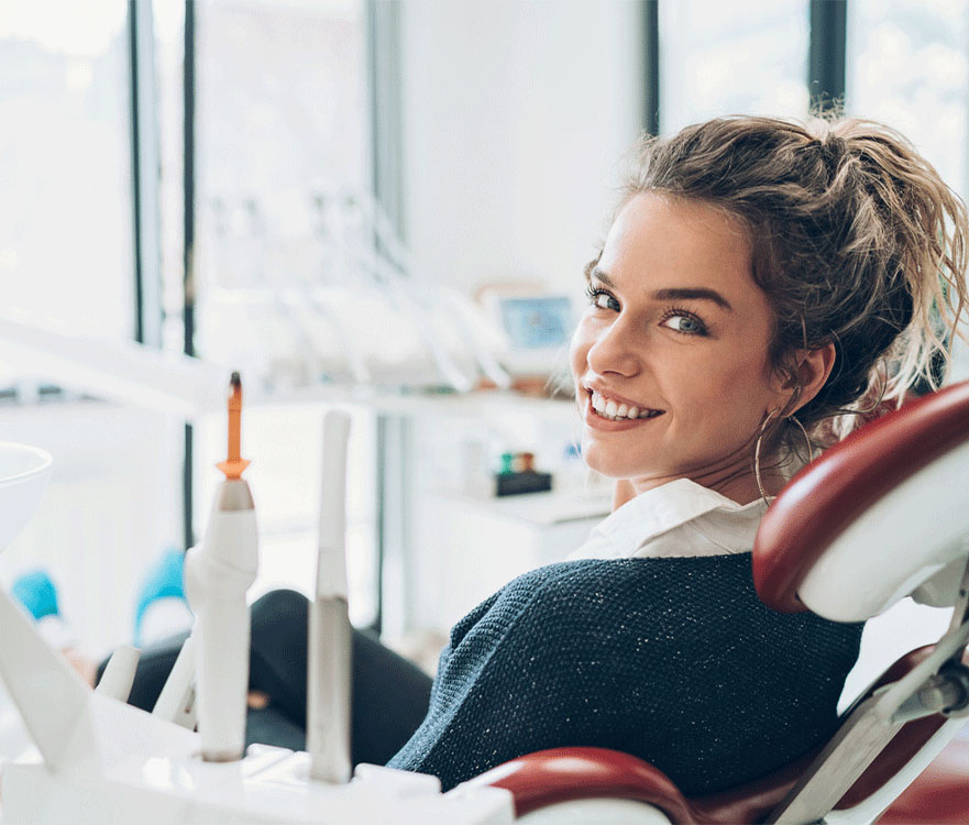 A young woman with a bright smile sits in a dental chair