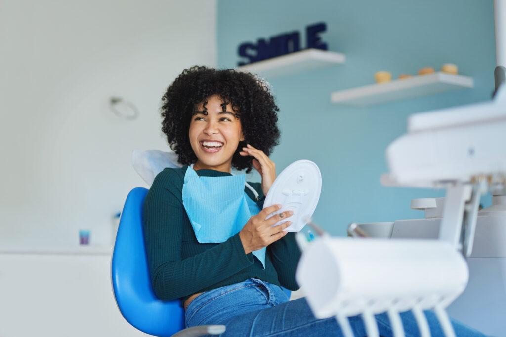 young woman with curly hair smiles brightly while sitting in a dental chair